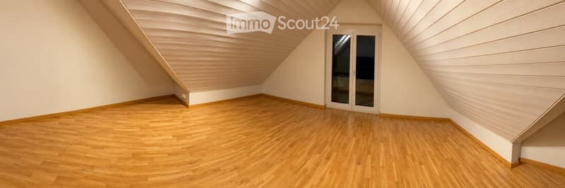 Empty attic room with wooden flooring, white walls, and a large window with glass panels.