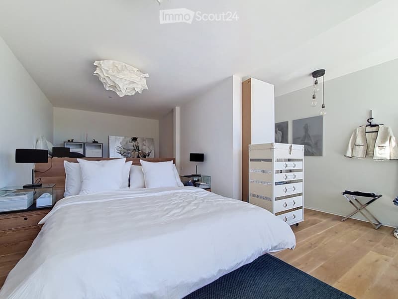 Modern bedroom with a large bed, nightstands, lamps, a chair, and artwork on the walls.