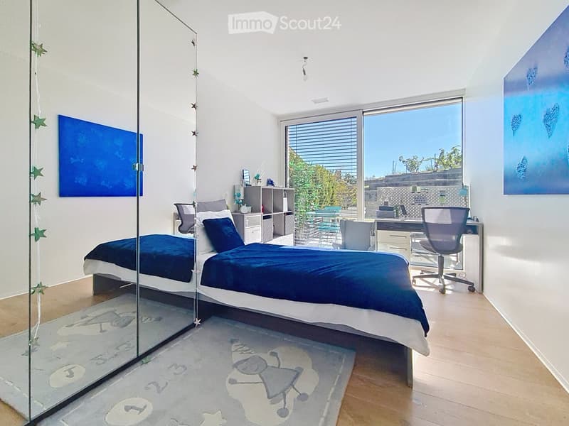 Modern bedroom with a large bed, desk, and chair, featuring large windows with blinds and artwork on the walls.