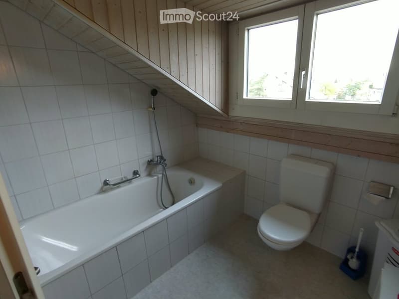 Bathroom with a white bathtub, toilet, tiled walls, and wooden trim. Features a window with a view and a handheld showerhead attached to the tub.
