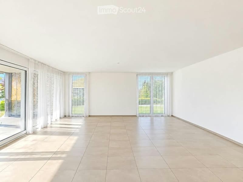 Empty room with white walls, tiled floor, large windows with sheer curtains, and sliding glass doors leading to an outdoor area.