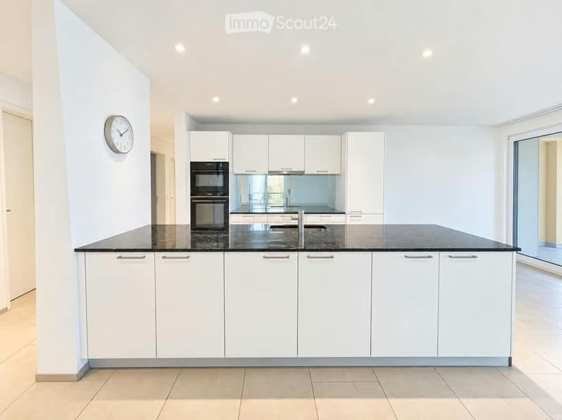 Modern kitchen with white cabinets, black countertop, built-in oven, and a clock on the wall.