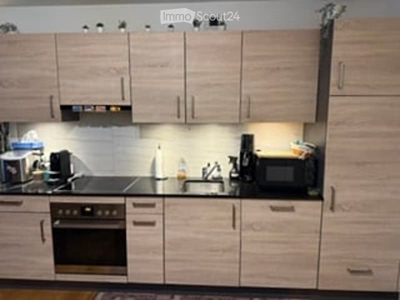 Modern kitchen with light wood cabinets, stainless steel appliances, and built-in lighting.