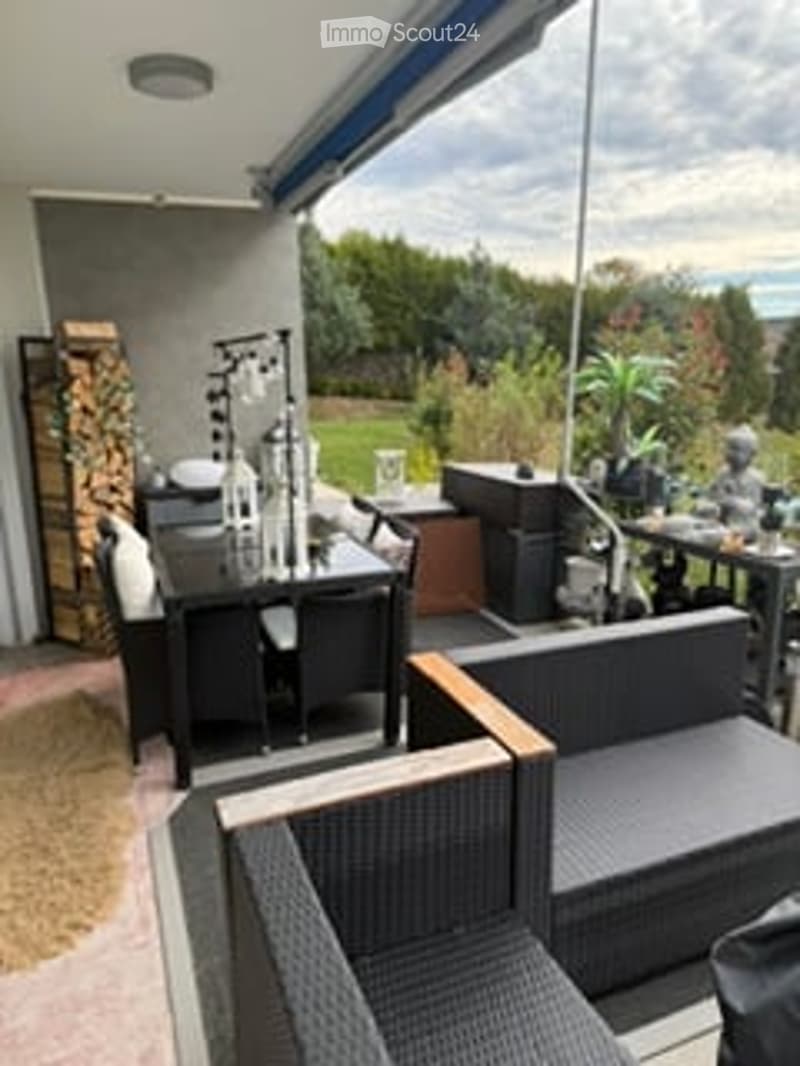 Outdoor patio with modern furniture, including a dining table, chairs, and a sofa. Features a wood stack, potted plants, and a covered area with a ceiling fan.