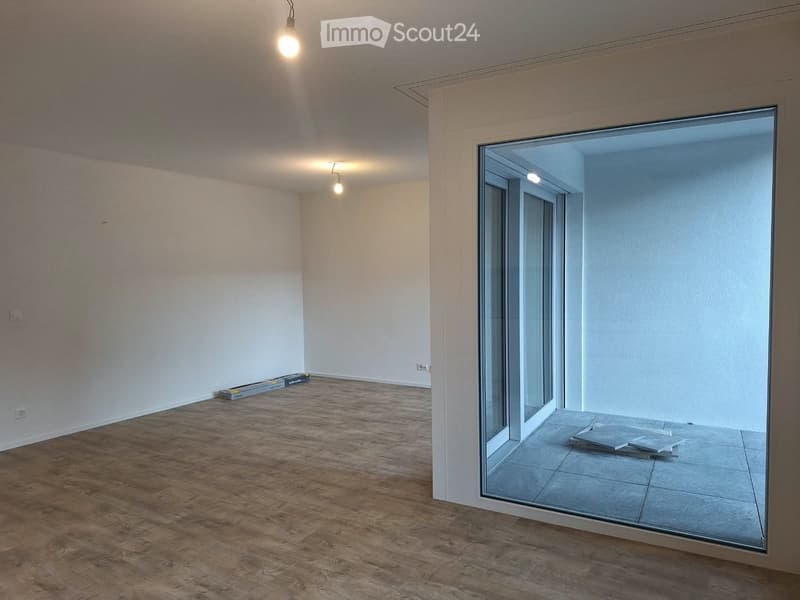 Empty room with wooden flooring, white walls, and large glass sliding doors leading to a tiled balcony area.