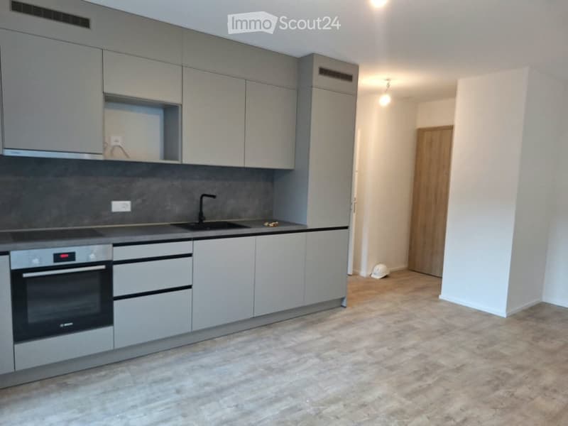 Modern kitchen with grey cabinets, stainless steel oven, sink, and faucet. Light-colored tiled floor and neutral walls.