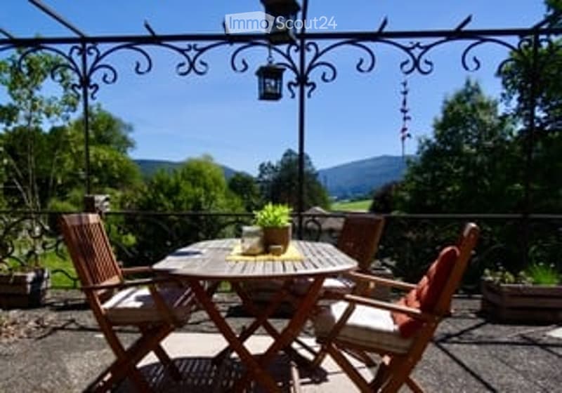 Wooden patio furniture set including a round table and four chairs, with a potted plant on the table, surrounded by a metal pergola with hanging lanterns.