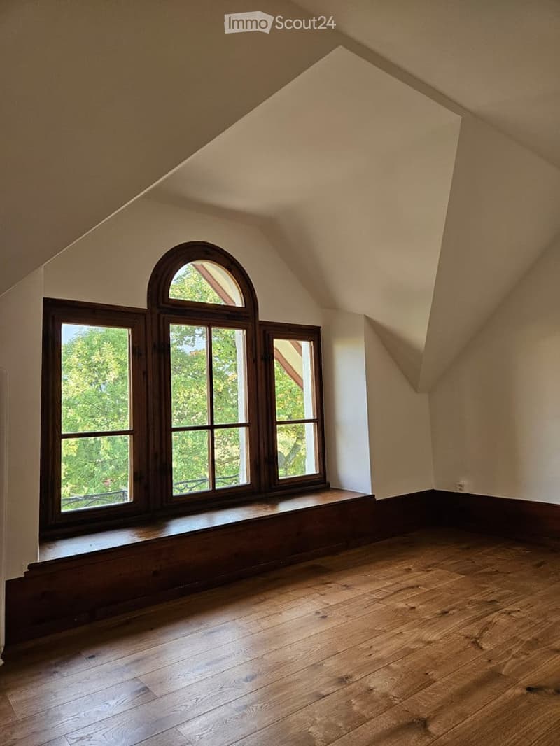 Empty attic room with wooden floors, large windows, and slanted ceilings.