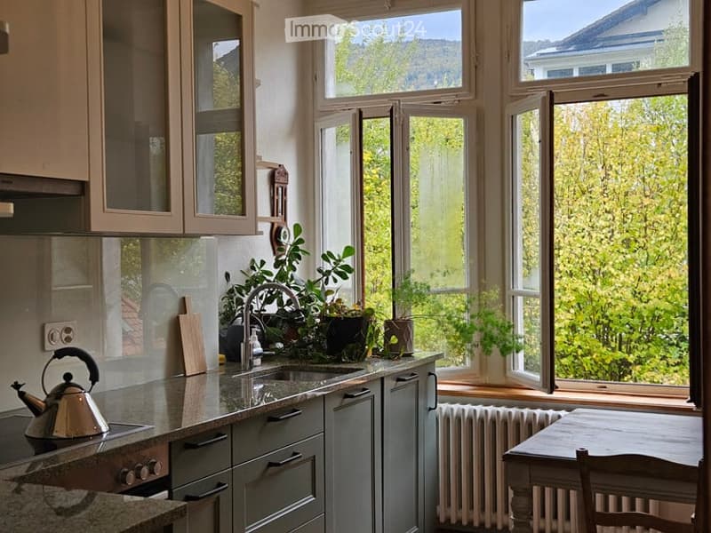 Bright kitchen with large windows, modern cabinets, granite countertops, and a small dining area.