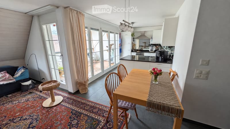 Bright living and dining area with large windows, a sofa, a dining table with chairs, a cat tree, and a kitchen area with appliances.