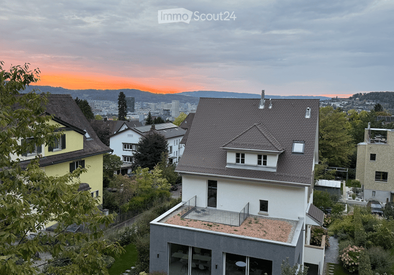 Modern multi-story house with a flat roof terrace, surrounded by greenery and other residential buildings, with a scenic cityscape view in the background.