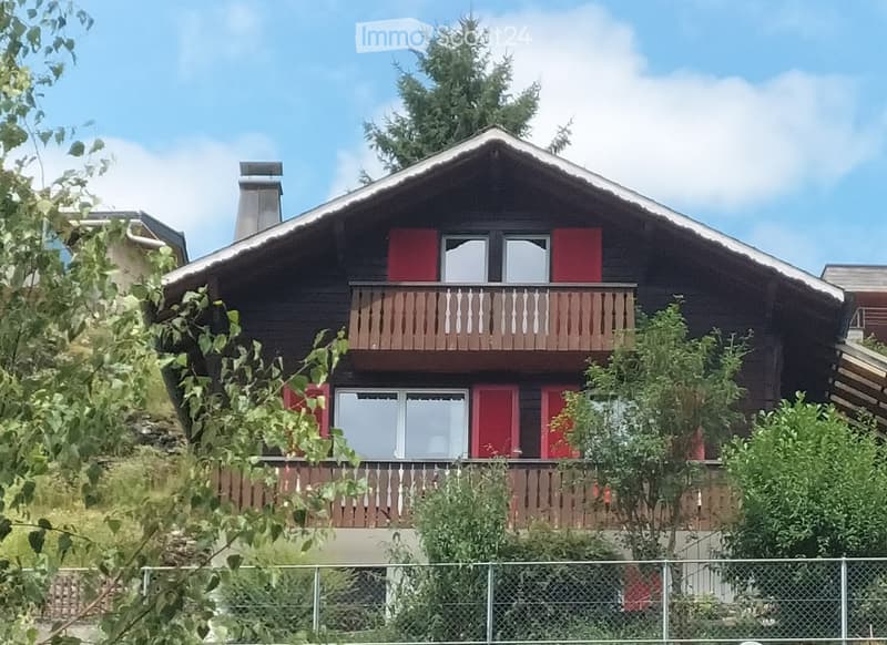Two-story wooden house with red shutters, multiple windows, and a balcony with wooden railing.