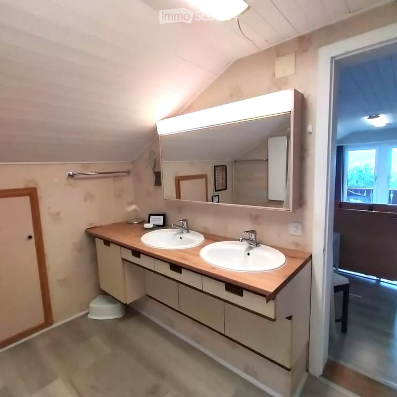 Bathroom with double sinks, wooden countertop, large mirror with built-in lighting, and a small stool under the cabinet.