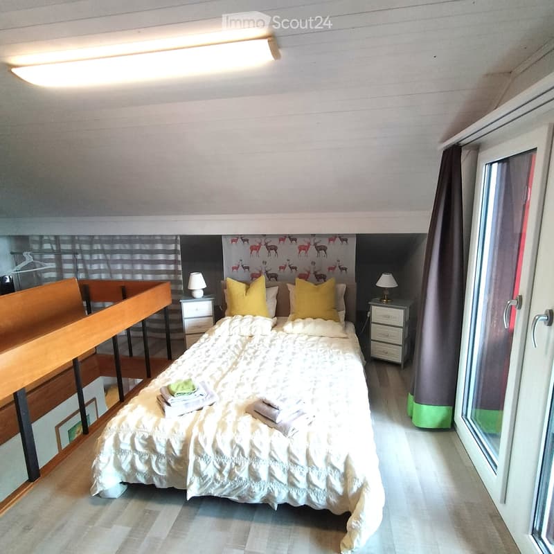 Cozy bedroom with a double bed, nightstands, lamps, and a large window with curtains. The bed is neatly made with pillows and blankets, and towels are placed on the bed.