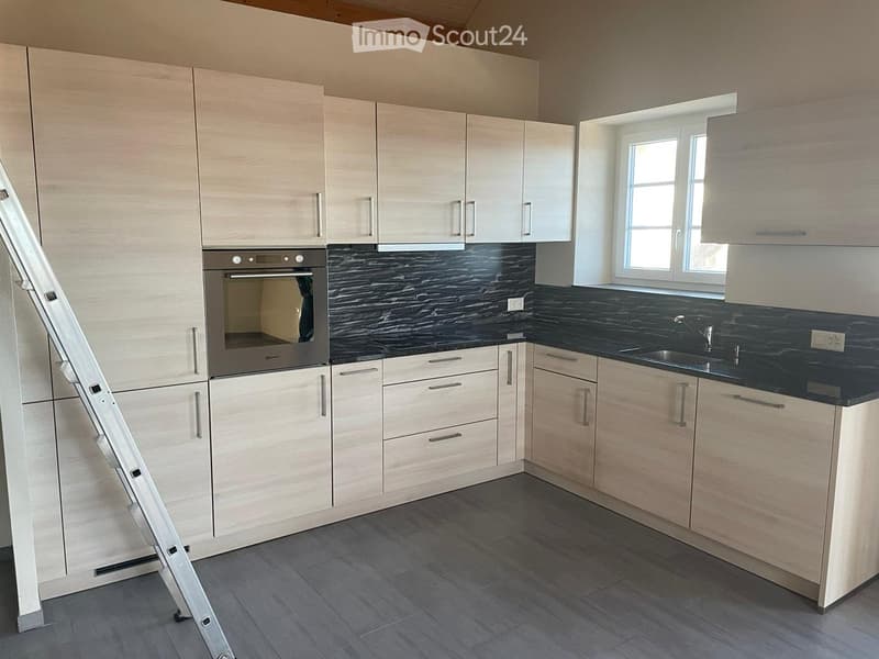 Modern kitchen with light wood cabinets, stainless steel oven, black countertop, and sink.