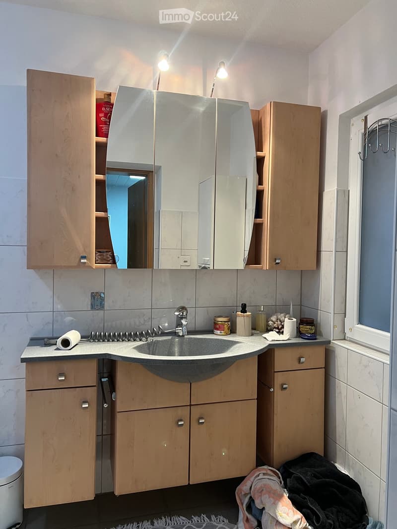 Bathroom with wooden cabinets, a sink, a mirror, and various toiletries on the counter.