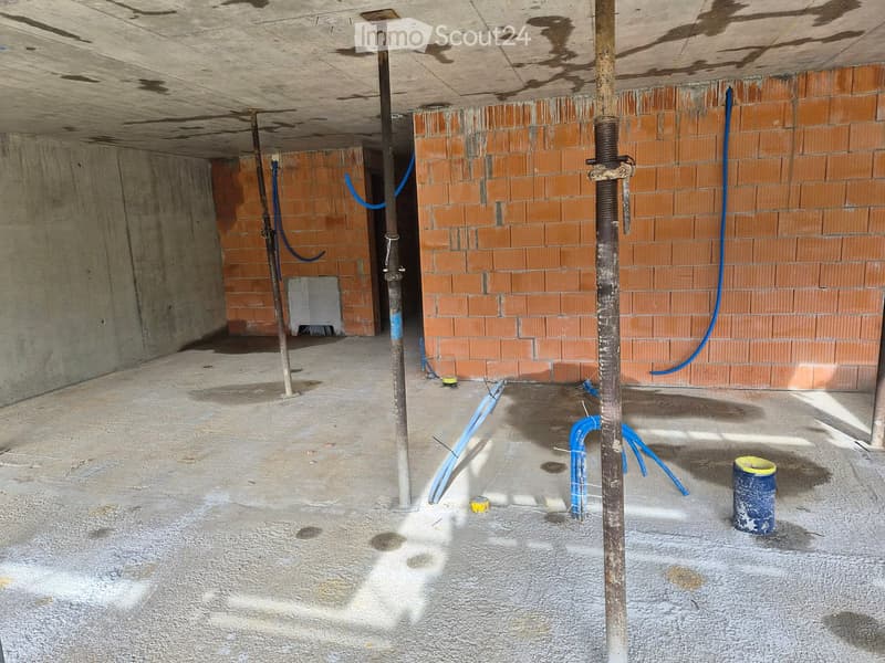 Empty basement or garage space with exposed brick walls, concrete floor, and various pipes and construction materials scattered around.