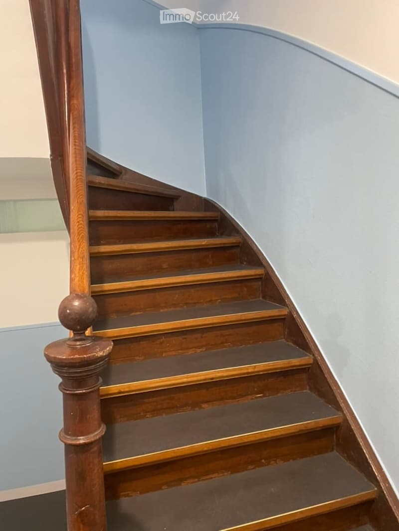 Spiral staircase with wooden steps and polished handrail, light blue walls, curved design.