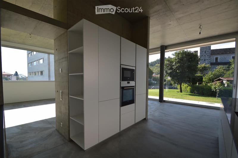 Modern kitchen with white cabinets, microwave, oven, and large windows overlooking a green area.