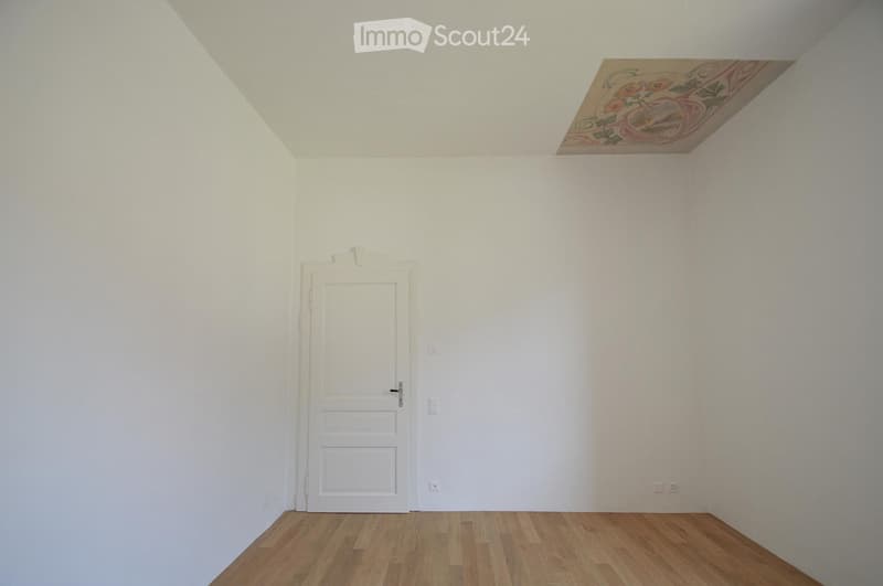 Empty room with white walls, wooden floor, and a single white door. No furniture or equipment present.