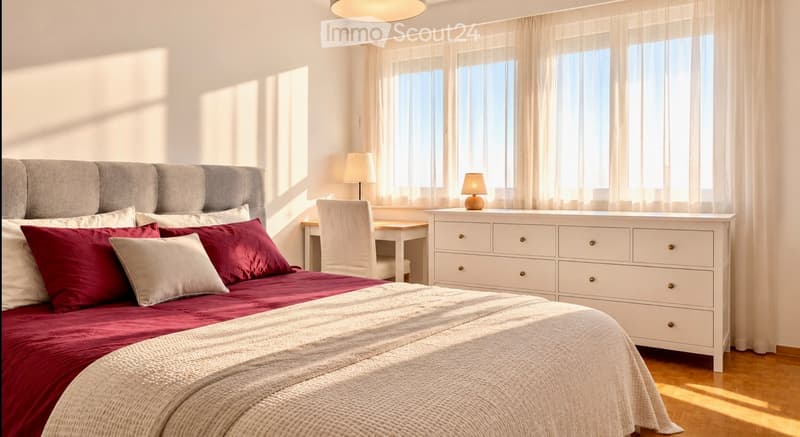 Modern bedroom with a large bed, red and white bedding, a grey headboard, a nightstand with a lamp, a small desk with a chair, and a white dresser with drawers.