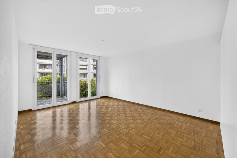 Empty room with wooden herringbone flooring, white walls, and large sliding glass doors leading to a balcony.