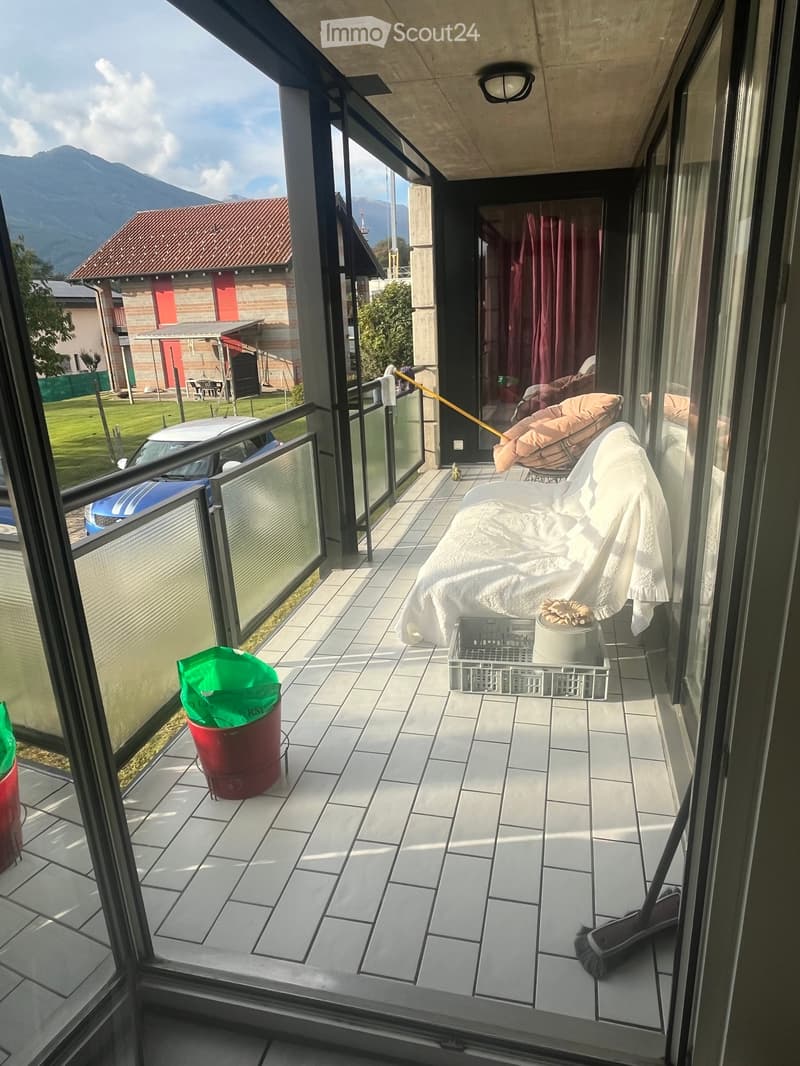 Balcony with tiled floor, sofa, small table with flower pot, trash bin, and broom visible. Offers a scenic mountain view.