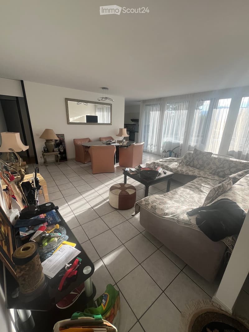 Living room with a sofa, coffee table, small round table, chairs, lamps, and a mirror. The room has tiled flooring and large windows with curtains.