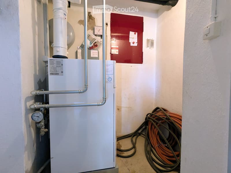 Utility room with a white boiler, metal pipes, and a coiled orange cable reel on the floor.