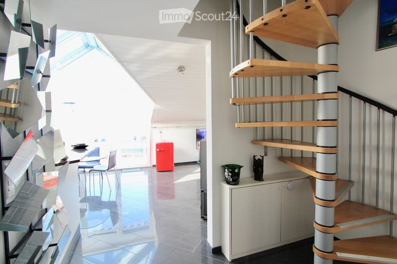 Modern interior with a sleek spiral staircase, a small table with chairs, and a red refrigerator in the background.