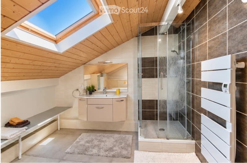 Modern bathroom with a skylight, wooden ceiling, glass shower enclosure, sink with mirror, and a bench with towels.