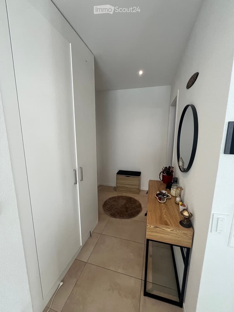 A small hallway with a wooden table, a round mirror, a storage box, and a round rug on the floor.