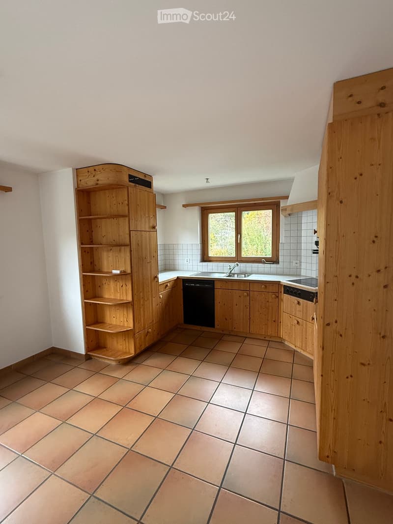 Bright kitchen with wooden cabinets, tiled floor, sink, dishwasher, and stove. Features a large window with a view of greenery.