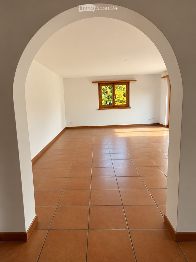 Empty hallway with arched ceiling, tiled floor, and a single window showing greenery outside.