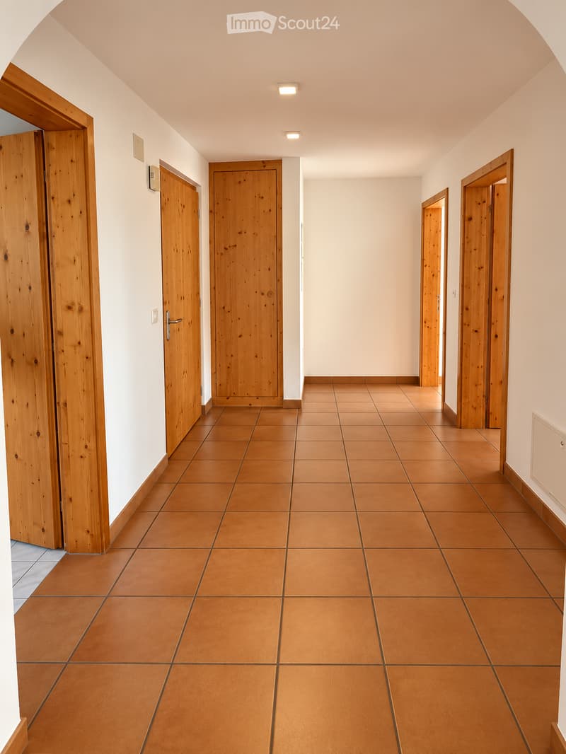 Empty hallway with wooden doors, tiled floor, and recessed lighting.