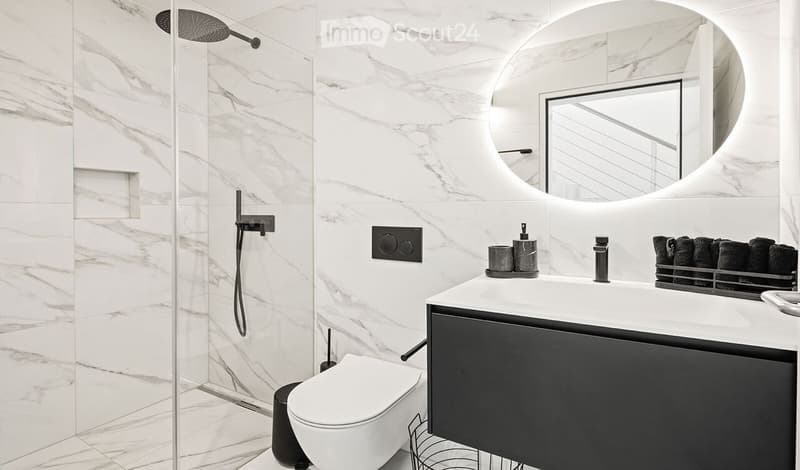 Modern bathroom with white marble tiles, a sleek sink with a black cabinet, a toilet, a glass-enclosed shower, and a large round mirror.