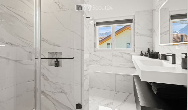 Modern bathroom with white marble tiles, a large window offering a scenic view, a double sink vanity, a bathtub, and a glass-enclosed shower.