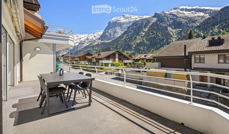 Balcony with a table and chairs, overlooking a scenic mountain view and village.