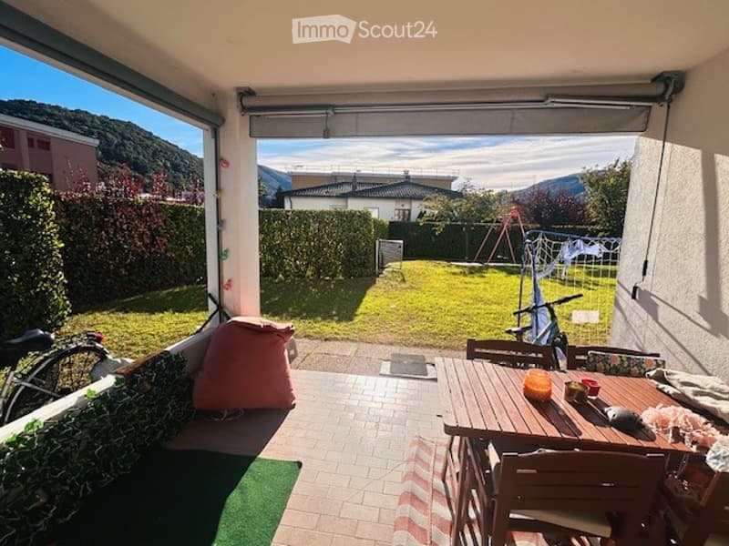 Balcony with outdoor dining table and chairs, overlooking a green garden and distant mountains.