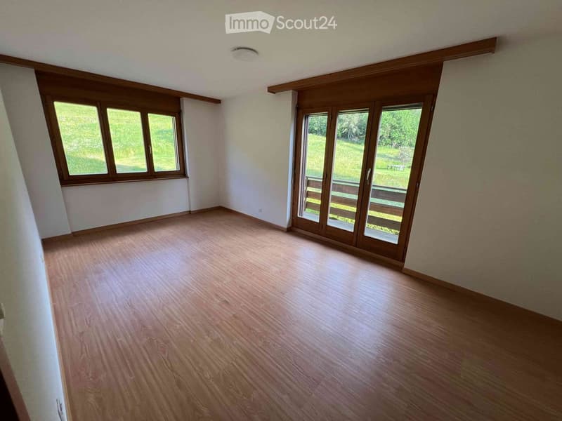 Empty room with wooden flooring, large windows, and sliding glass doors leading to an outdoor area.