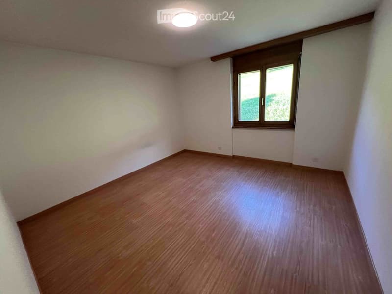 Empty room with wooden flooring, white walls, and a single window with wooden frame. The ceiling has a recessed light fixture.