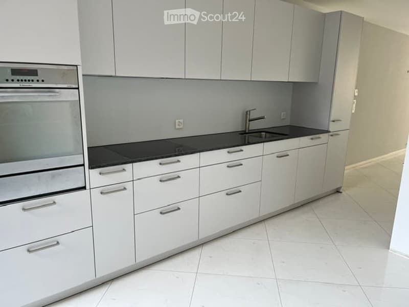 Modern kitchen with white cabinets, black countertops, and stainless steel appliances including an oven and sink.
