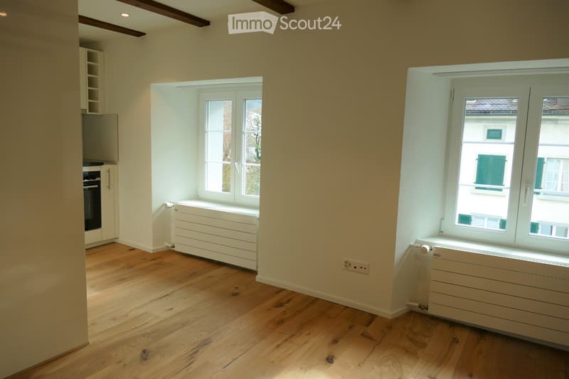 Empty room with wooden flooring, white walls, and large windows. No furniture or equipment present.