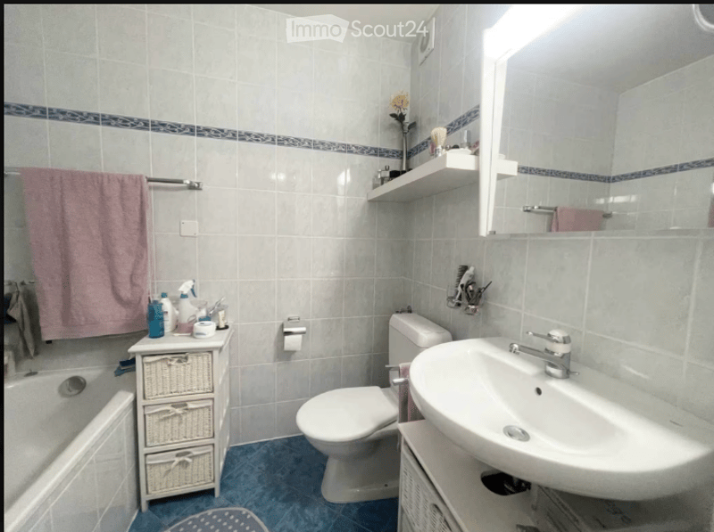 Bathroom with white tiles, blue accents, a bathtub, toilet, sink, mirror, and a small shelf with toiletries.