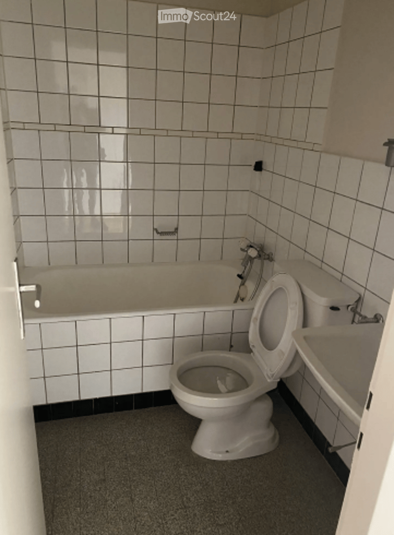 Bathroom with white tiled walls and floor, featuring a bathtub, toilet, and sink.