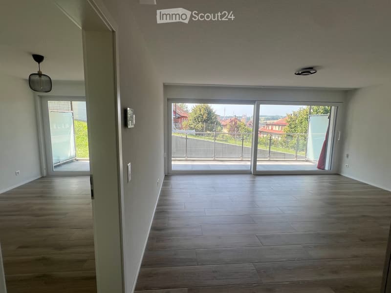 Empty hallway with wooden flooring, white walls, and large sliding glass doors leading to a balcony area.