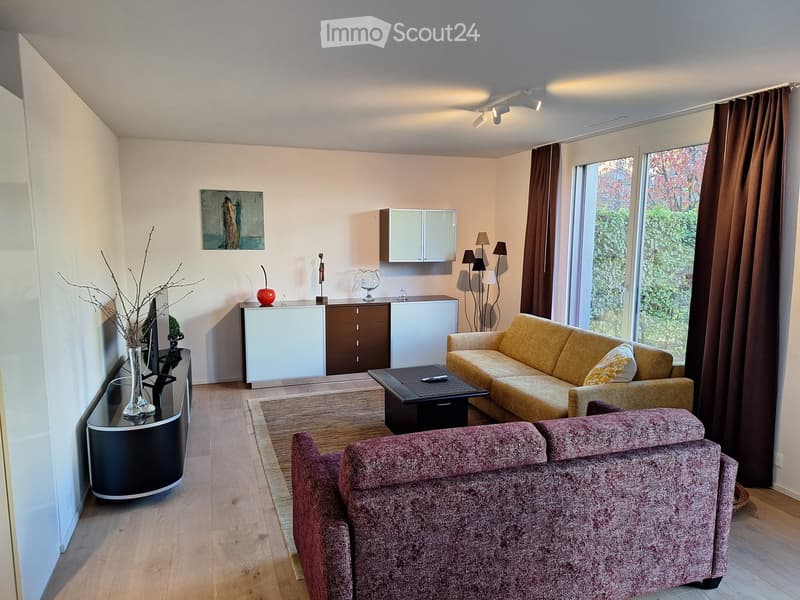 Modern living room with light wooden flooring, large windows with brown curtains, a yellow sofa, a red armchair, a black coffee table, a white cabinet, and decorative items including a vase with branches and a picture frame on the wall.
