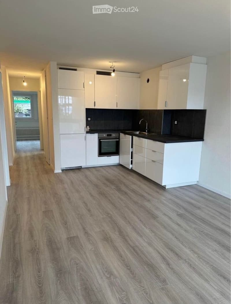 Modern kitchen with white cabinets, black countertops, and a stainless steel oven. Wooden flooring and a window provide natural light.