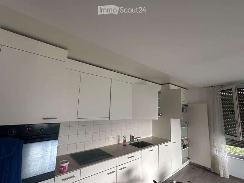 Modern kitchen with white cabinets, stainless steel sink, and oven. Countertop has a few items including a container and a bottle.