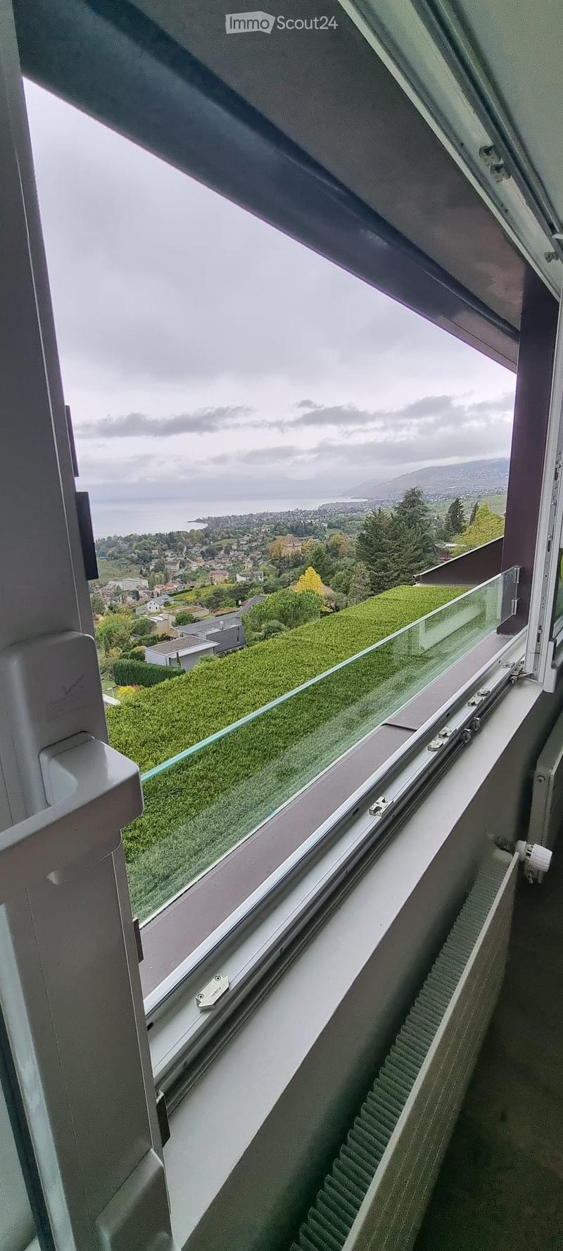 View from a balcony showing a scenic landscape with a lake, town, and hills in the background.
